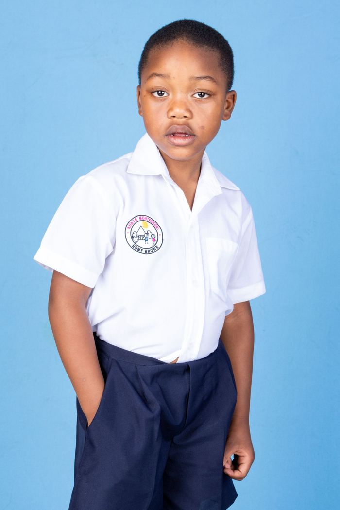 A Khaya Montessori learner in a white shirt with the Home Grown crest